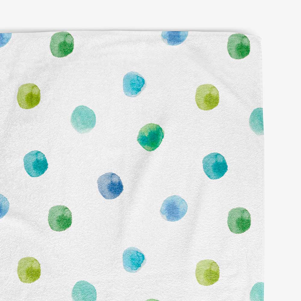 Close-up view of the soft texture and vibrant blue and green watercolor polka dots on a white cotton polyester velour bath towel.